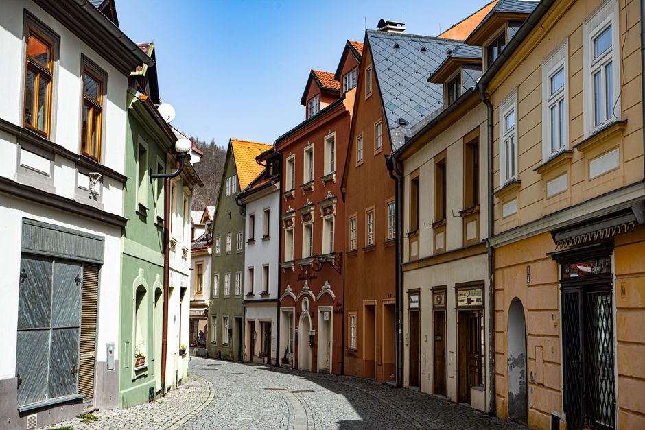 A picturesque cobblestone street with colorful historic houses in a European town — the kind of emerging micro-neighborhood where property values are 30–50% lower than the main tourist zone, yet tourists actively seek out for authentic stays.