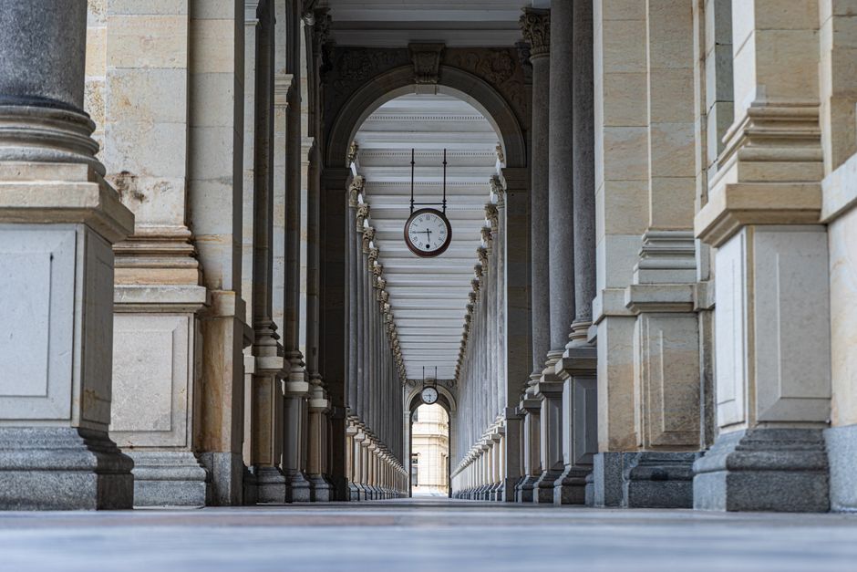 Vista simétrica de una columnata histórica con relojes colgando del techo.