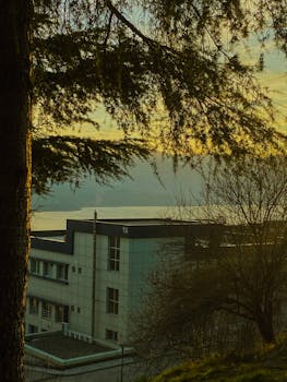 A tranquil view through trees of a building and lake at sunset in Türkiye.