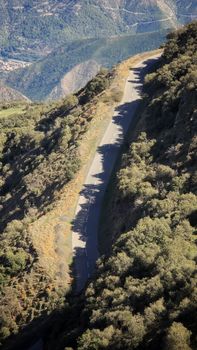 Aerial view of a winding mountain road with dramatic tree shadows and lush greenery.