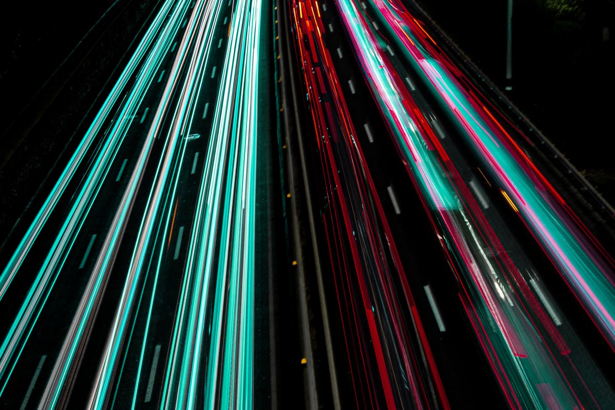 Long exposure of a highway at night with teal and red light trails from fast-moving traffic