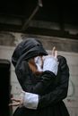 一个戴着兜帽、身着深色衣服的人，在阴森的废弃环境中摆出姿势