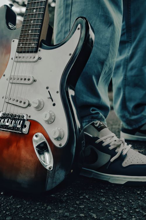 Free Stylish close-up of an electric guitar next to casual sneakers on a street. Stock Photo