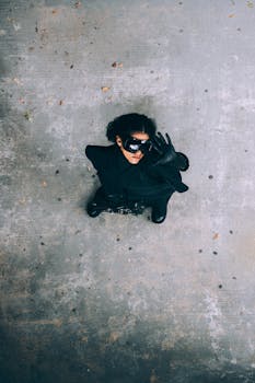 A person in a black costume and mask, viewed from above, stands on a textured surface.