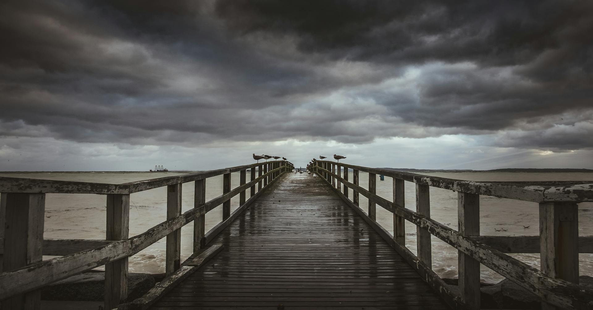 Gloomy seascape with a wooden pier leading into the Baltic Sea under ominous clouds.