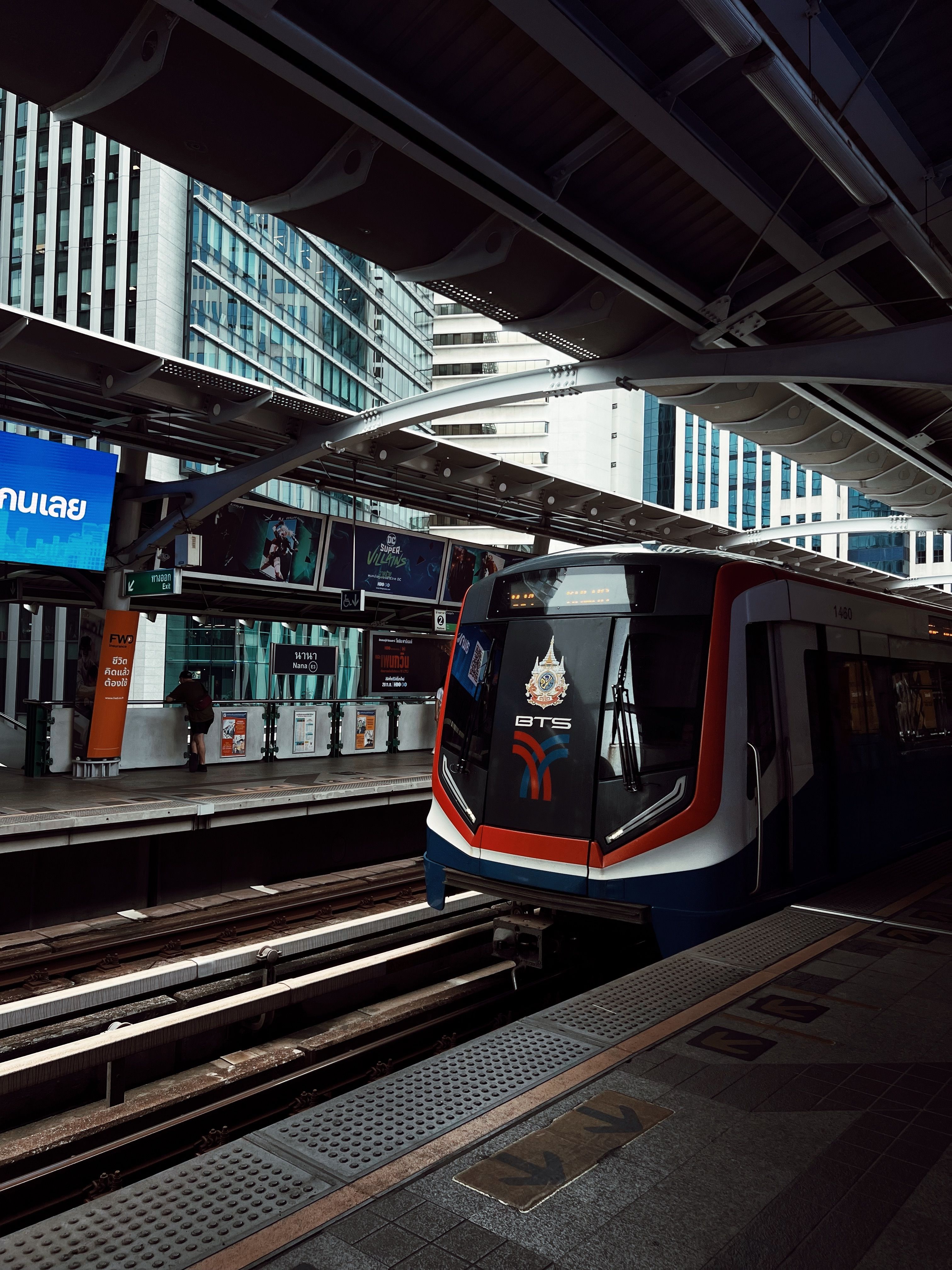 BTS Skytrain arrives at Bangkok station amidst urban high-rise buildings.