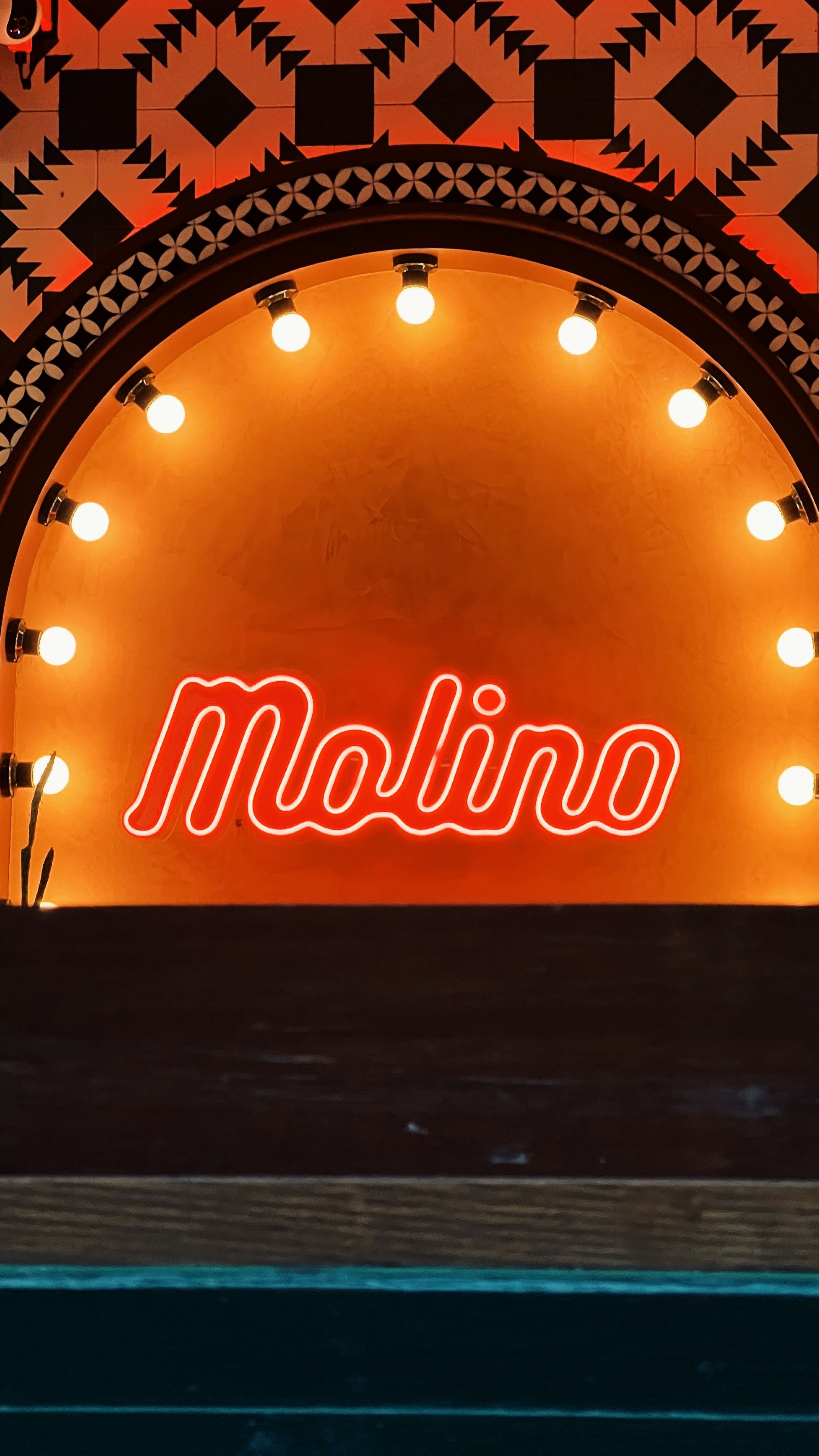 A warm vintage-style neon sign reading 'Molino' with surrounding light bulbs and patterns.