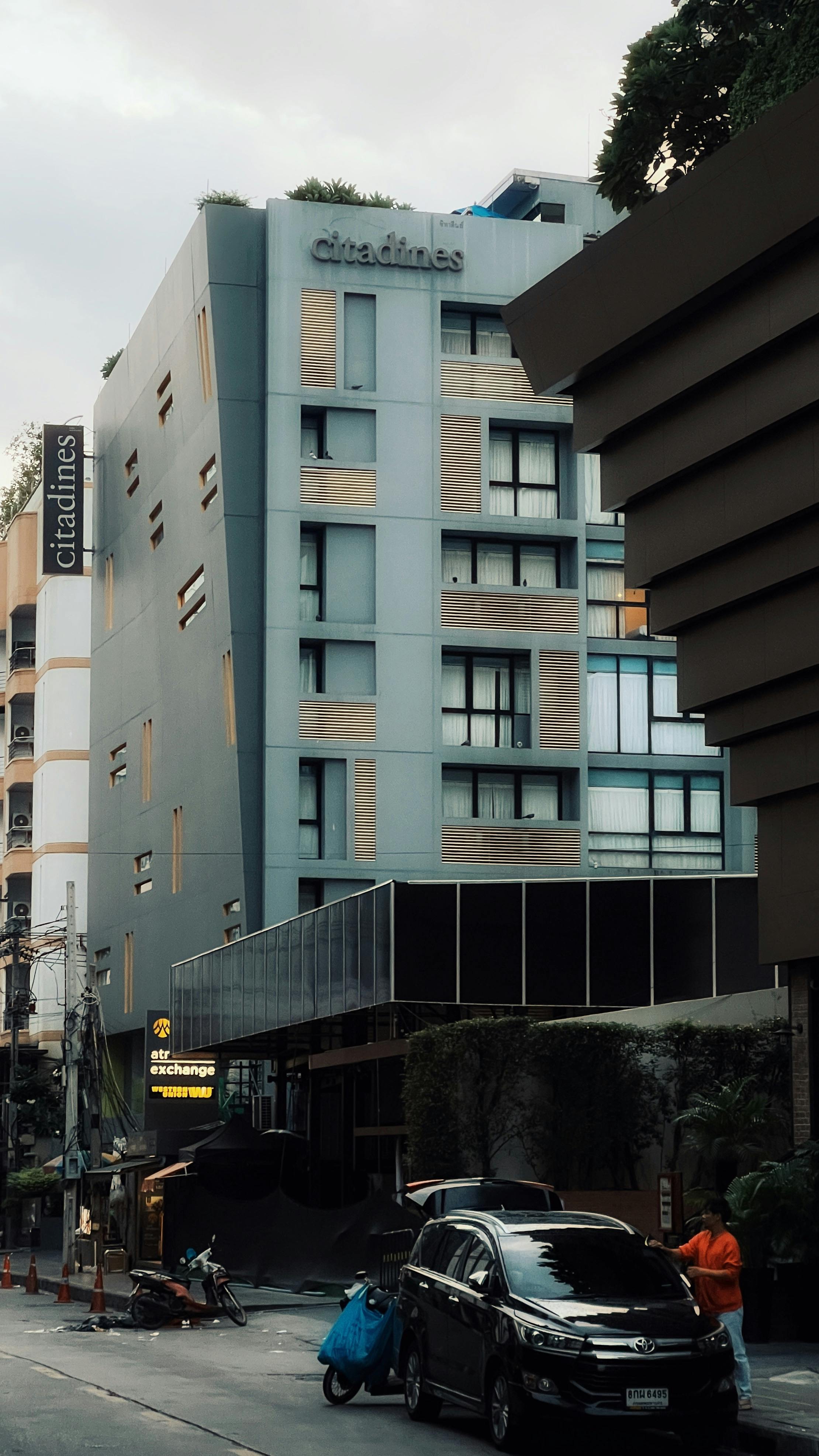 Street view of a modern city hotel with parked vehicles and pedestrians.