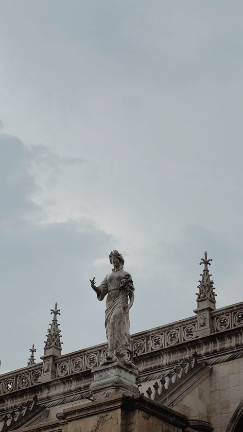 Free A majestic marble statue on an ornate building facade under a cloudy sky. Stock Photo