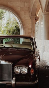A vintage Rolls-Royce parked under an elegant stone archway with lush greenery.