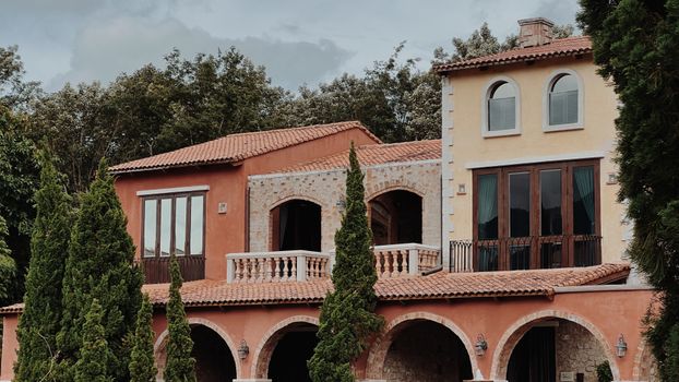 Mediterranean-style house with arched windows and vibrant facade nestled among tall trees.