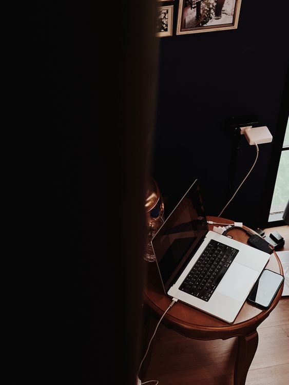 Home office compacto com notebook, celular, carregadores e tomada visível na parede