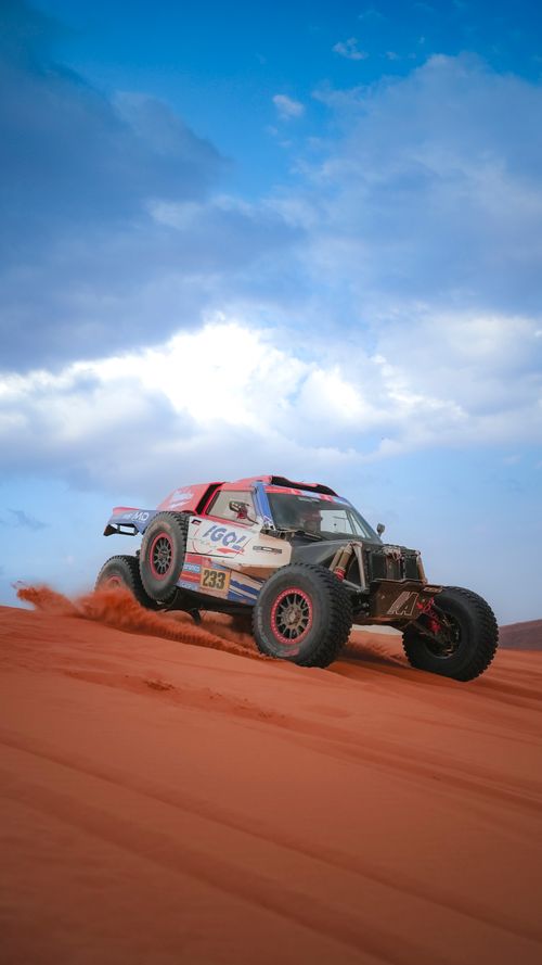 Free Rugged off-road rally car powers through sandy desert dunes under a bright blue sky. Stock Photo