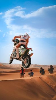 Dynamic shot of a motorcyclist performing a jump over sand dunes in a desert landscape.