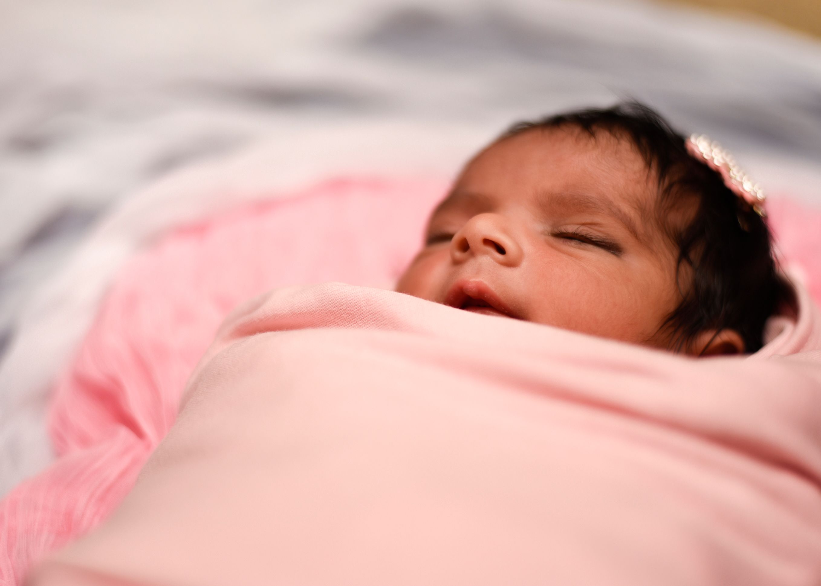 A serene image of a newborn baby wrapped in a soft pink blanket, peacefully sleeping.