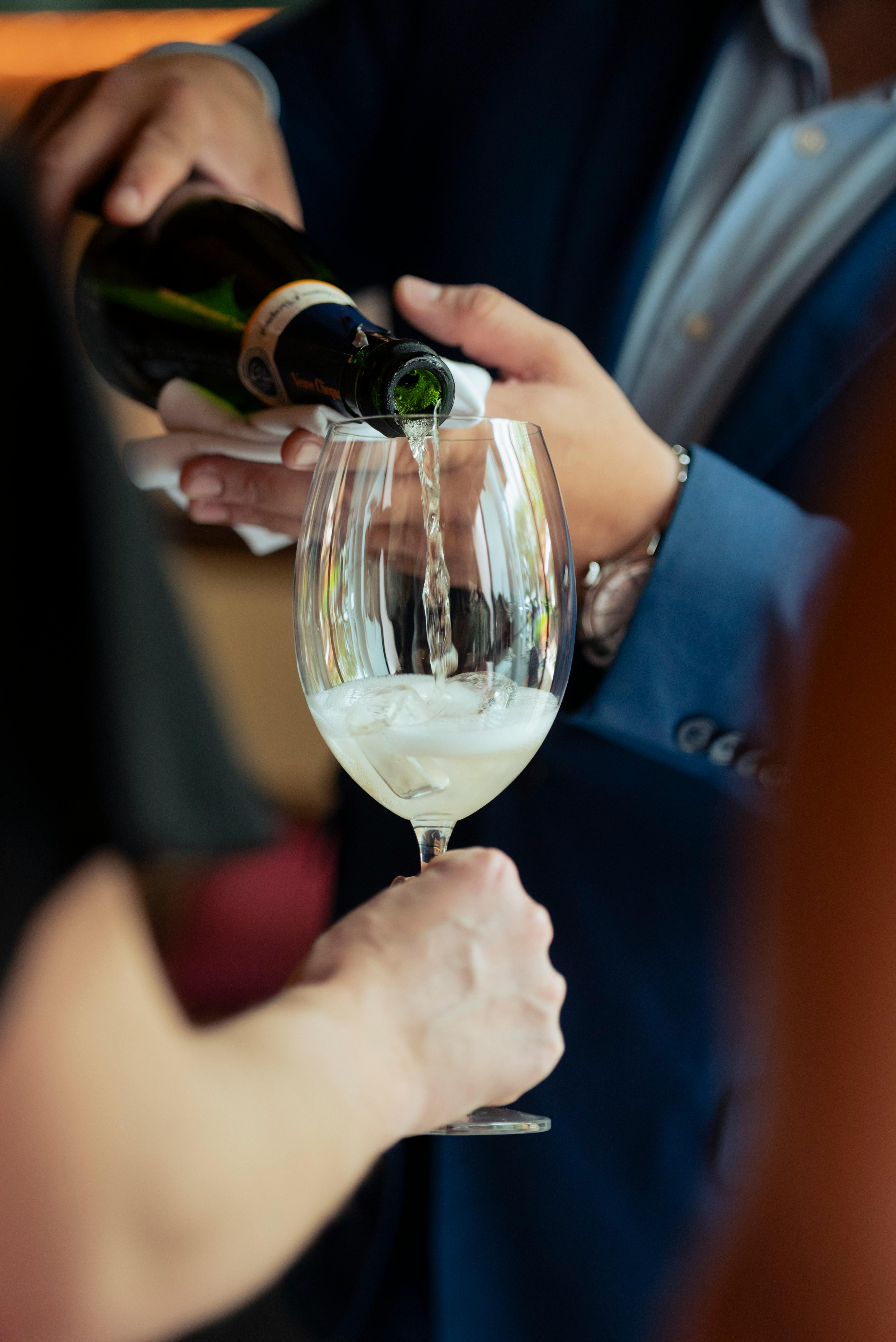 A person in formal attire pouring champagne into a glass.