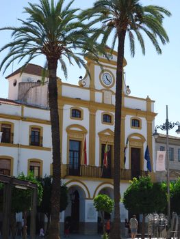 Elegant Mediterranean building facade flanked by palm trees under a sunny sky.