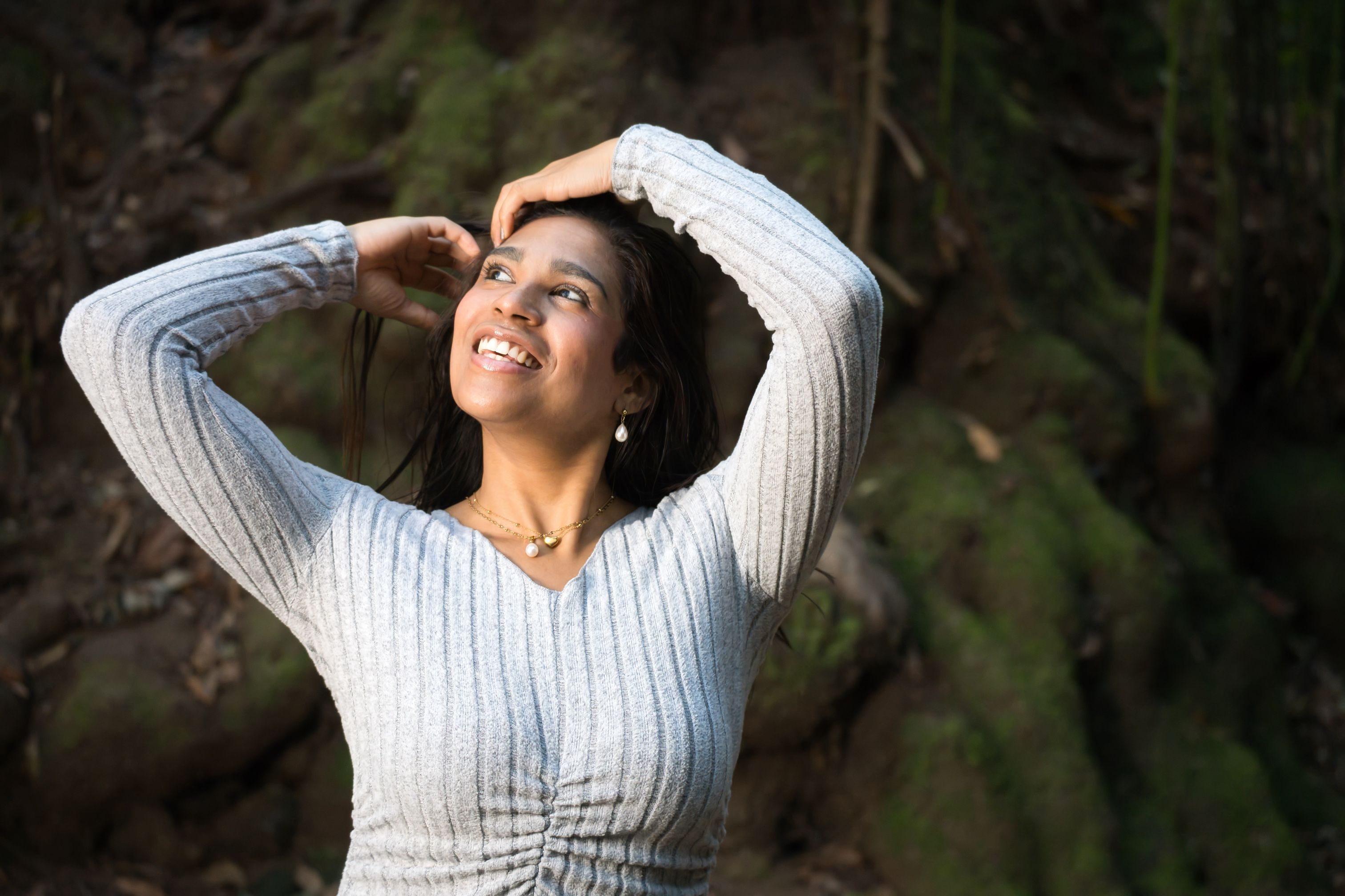 A joyful woman in a gray sweater enjoying a sunny day outdoors.