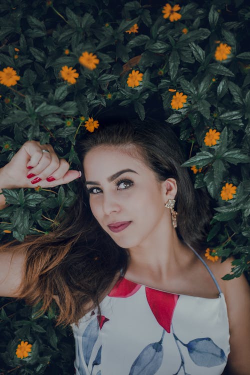 Femme Portant Un Haut Imprimé Blanc, Bleu Et Rouge Allongé Sur Un Lit Fleurs Jaunes Avec Des Feuilles Vertes