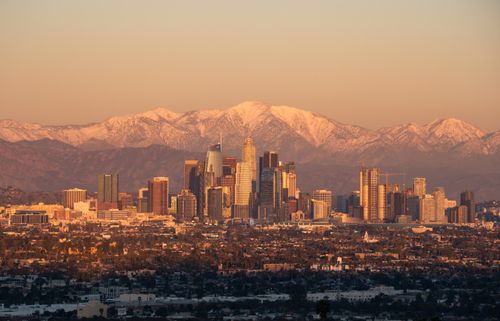 Free Stunning Los Angeles skyline during golden hour with snow-capped mountains in the background. Stock Photo