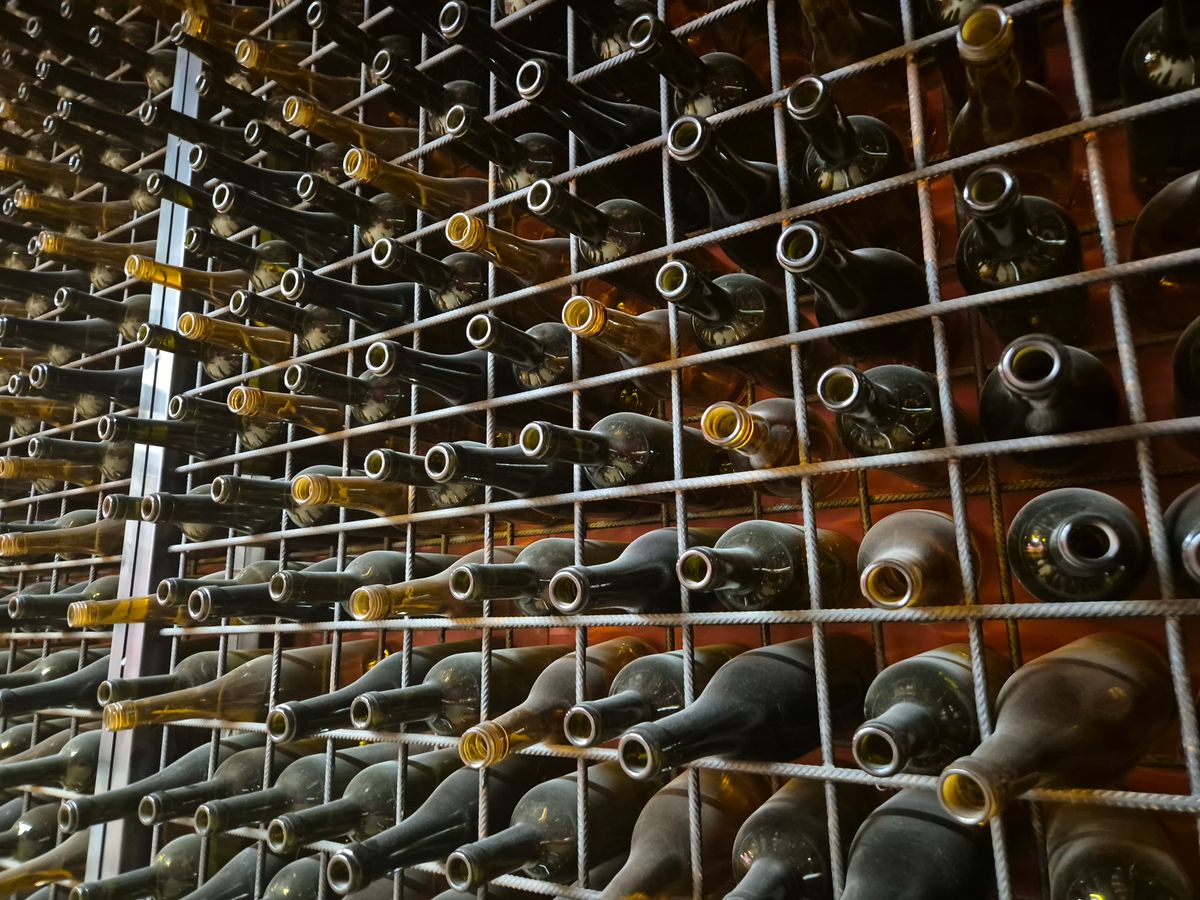 Rows of unlabeled wine bottles binned in a metal storage rack in a cellar, representing landed U.S. wine inventory