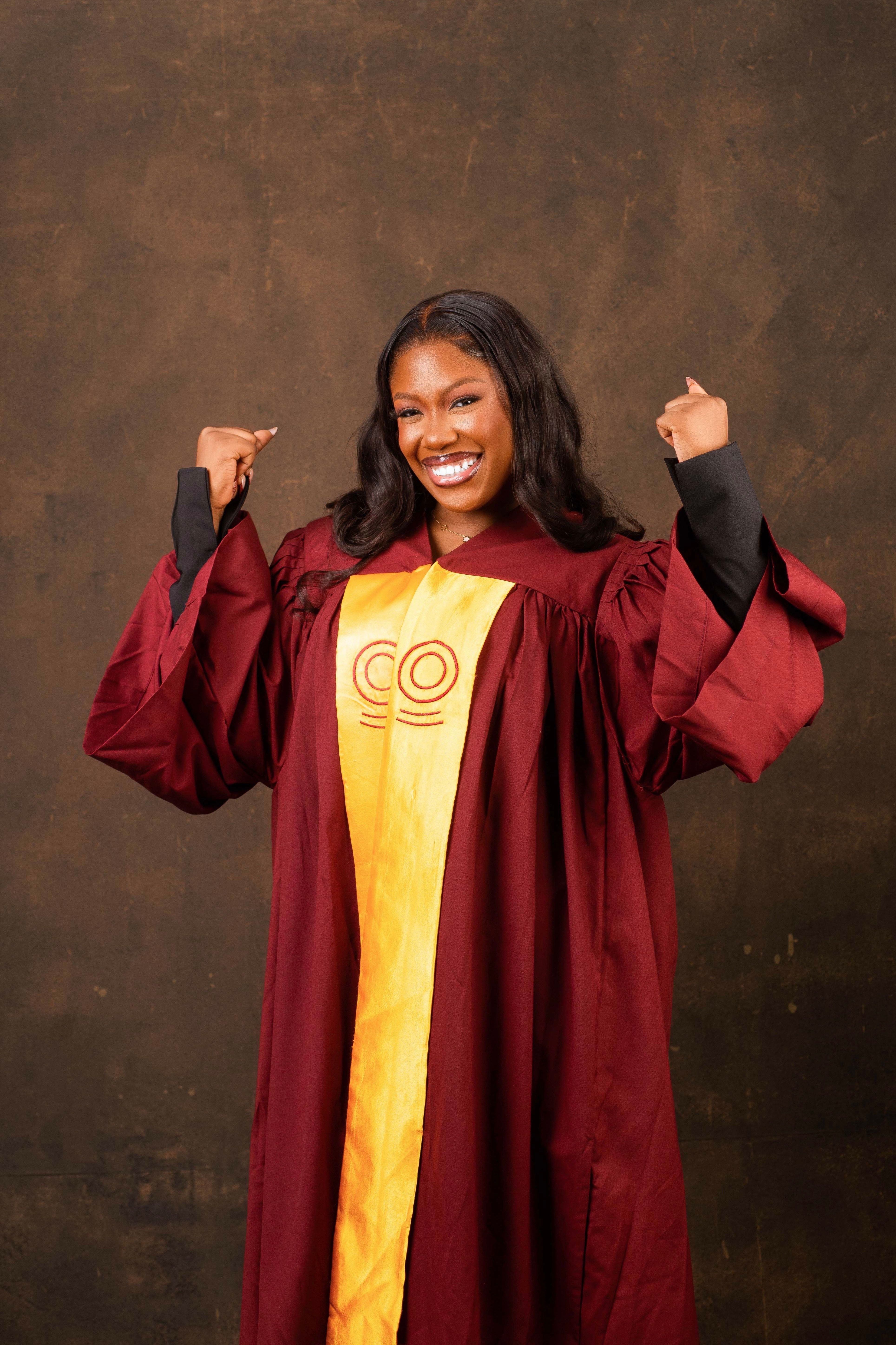 A young woman happily celebrating her graduation in a maroon gown.