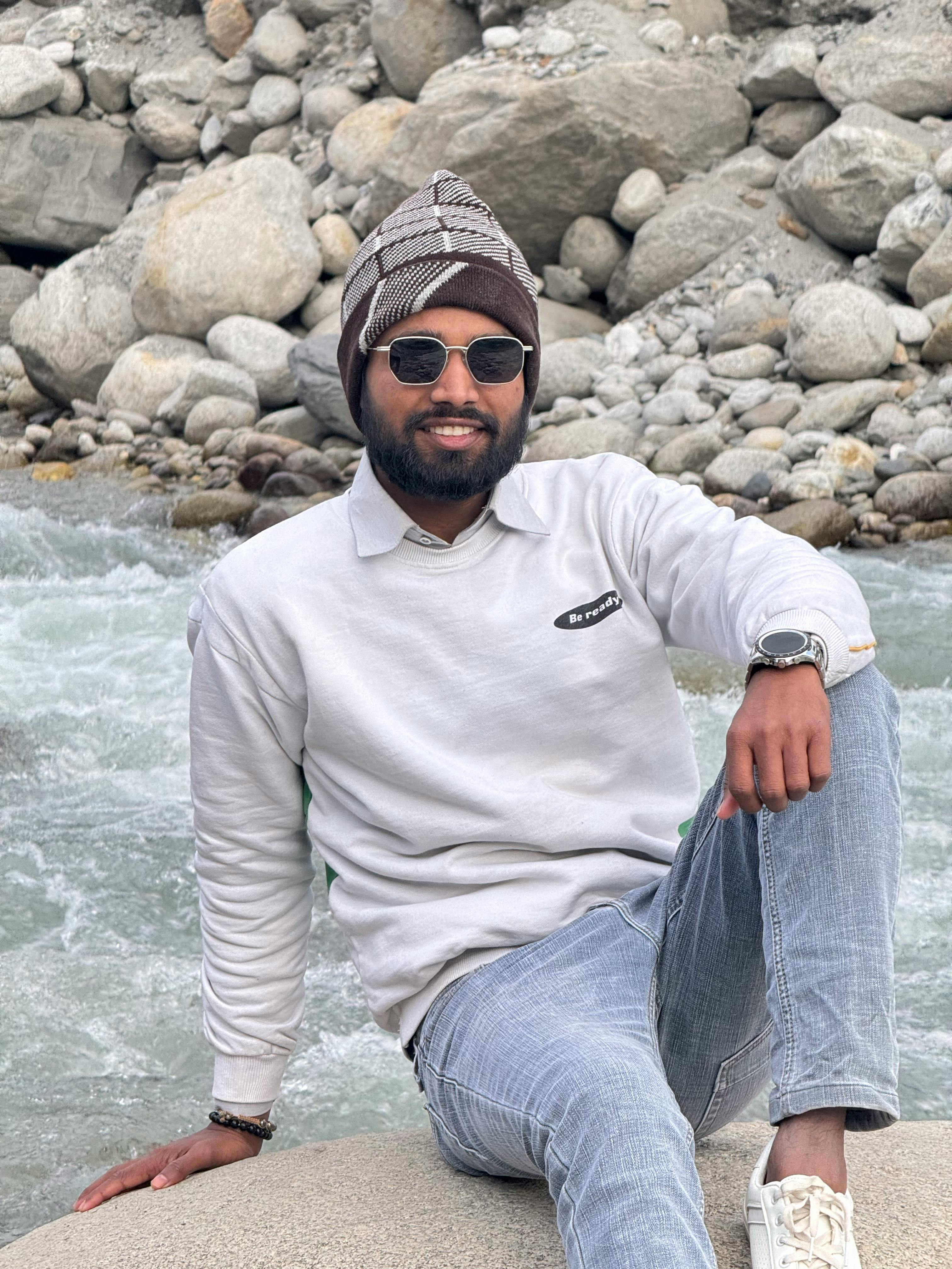 Man in casual wear sitting on rocks by a flowing mountain stream, outdoors.