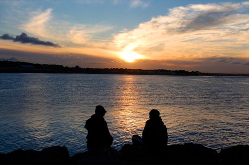 Free Two people silhouetted against a vibrant seaside sunset, capturing tranquility and beauty. Stock Photo