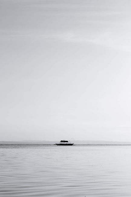 Minimalist black and white photo of a solitary boat on the ocean viewed from the Philippines coastline.