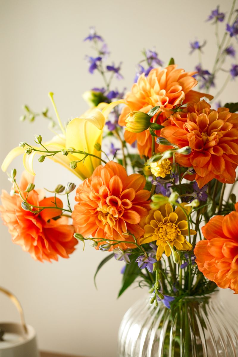 Bright bouquet of orange and yellow flowers, including dahlias, in a vase indoors.