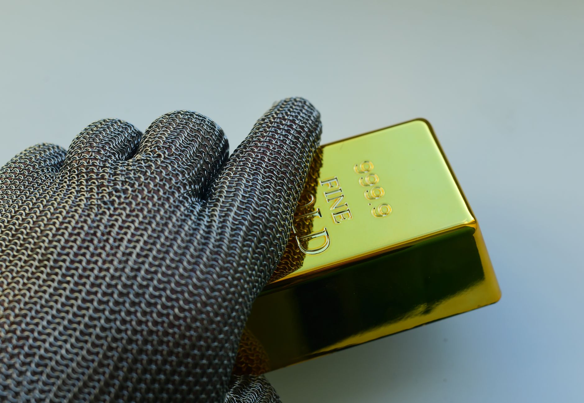 Close-up of a metal gloved hand holding a shiny gold bar indoors.