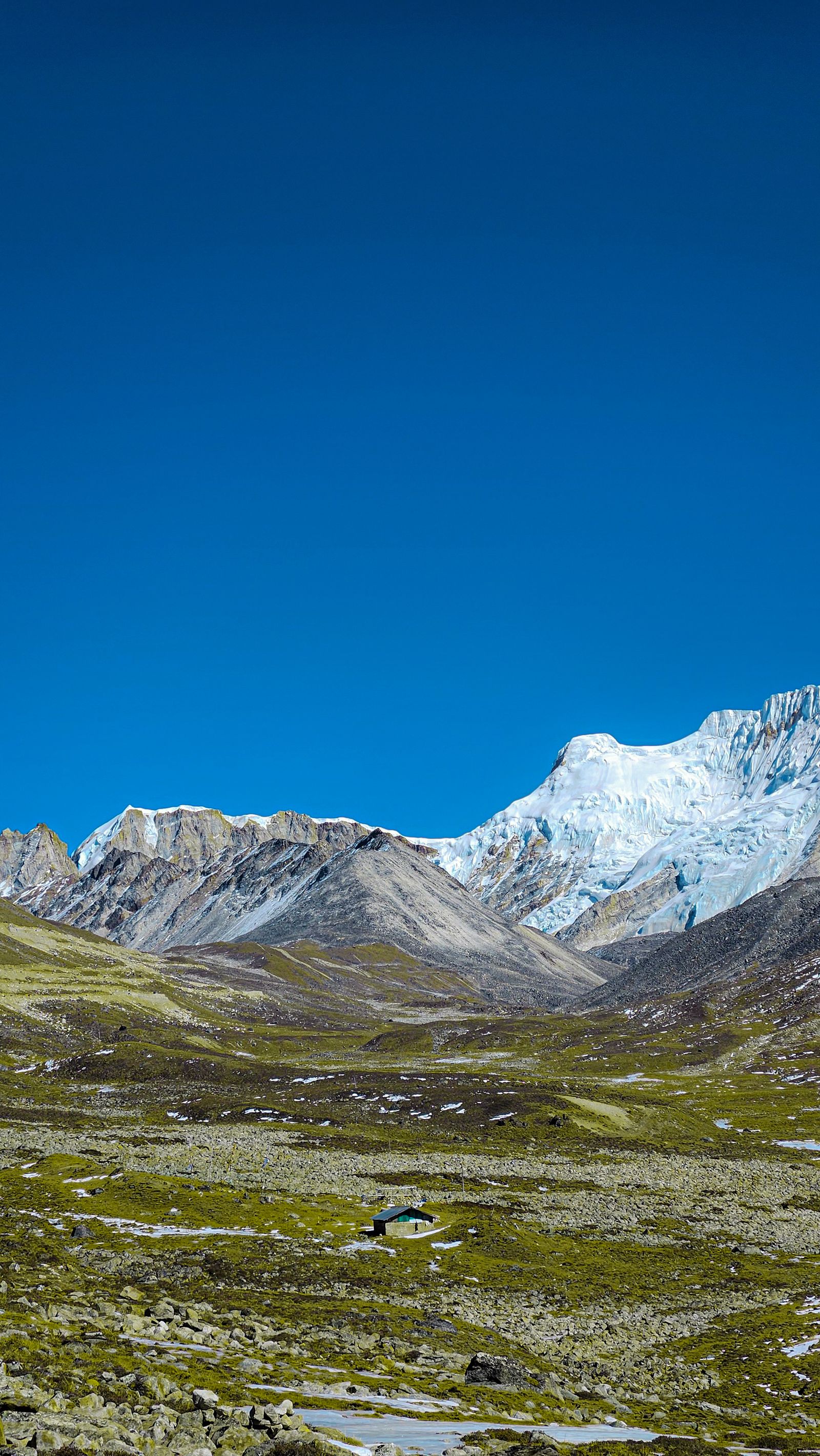 A high alpine basin in Sikkim above the treeline, a small stone hut below a glaciated snow peak and bare ridges