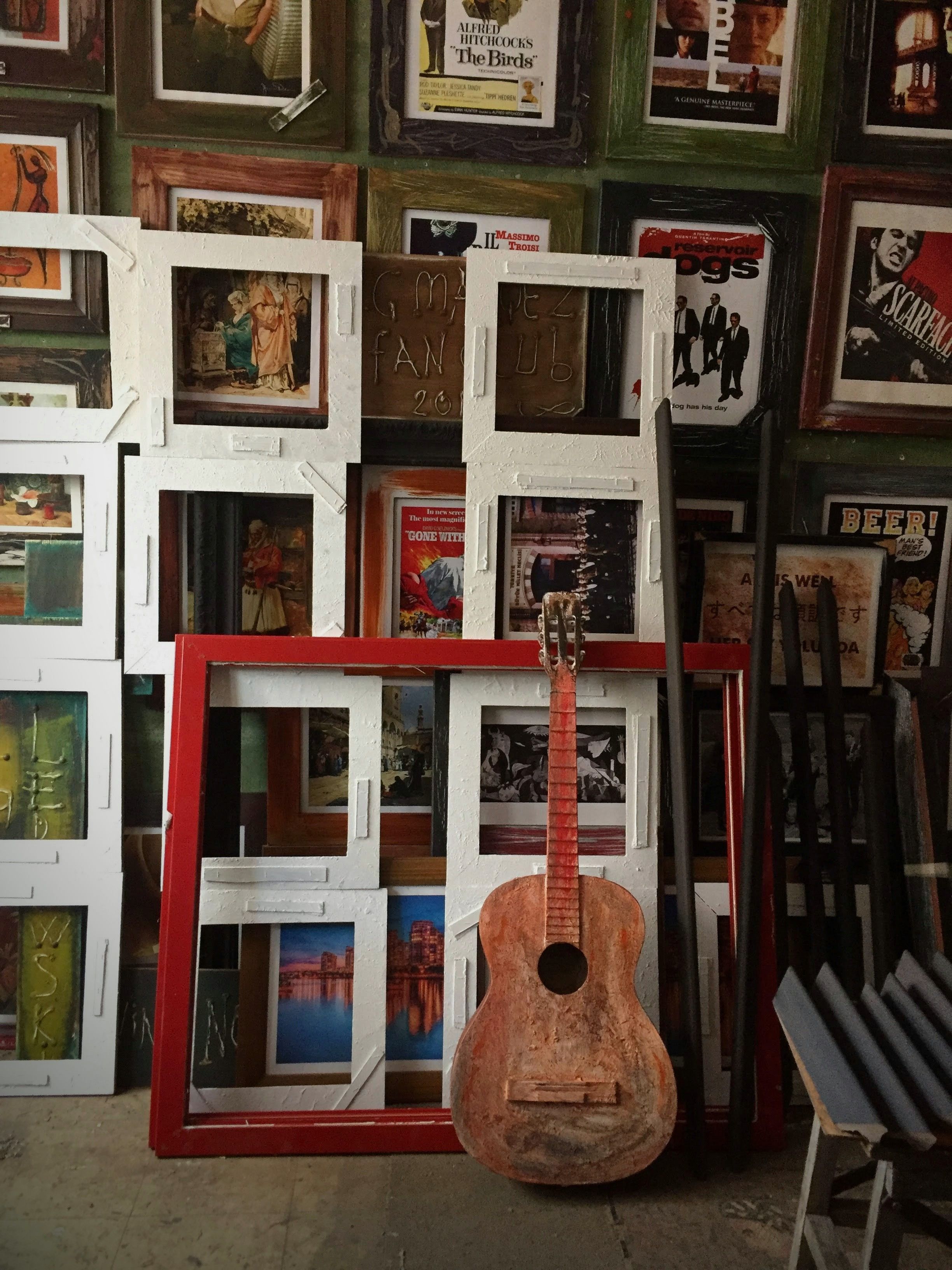 A rustic guitar and colorful picture frames on display in an artsy studio setting.
