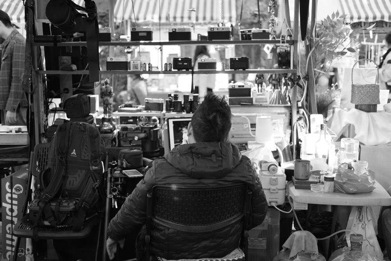 A person in a shop full of vintage cameras captured in black and white.