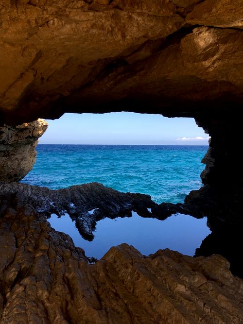 Free A breathtaking view of the deep blue sea framed by rugged rock formations and natural cave opening. Stock Photo