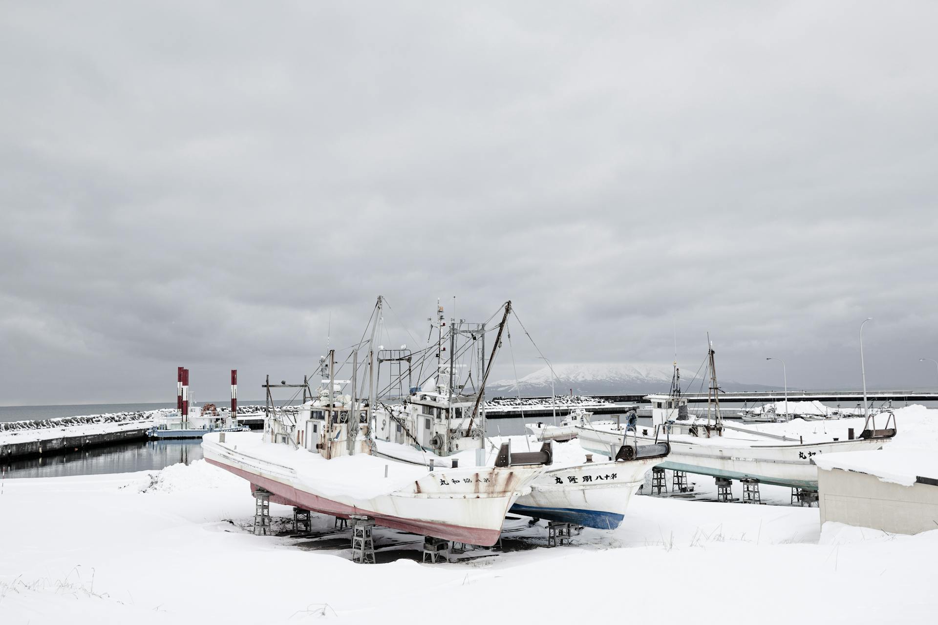 Fishing boats covered in snow at a harbor on a cloudy winter day.
