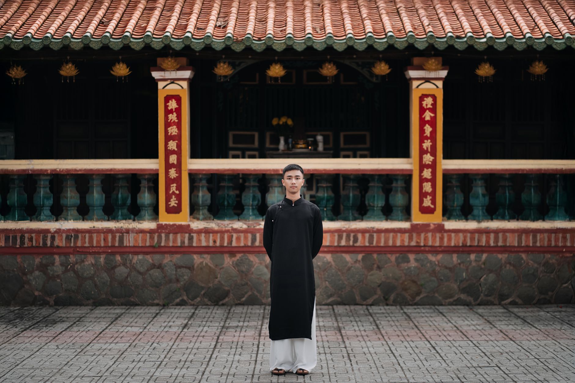 Young man in traditional attire standing before a historic temple with cultural elements.