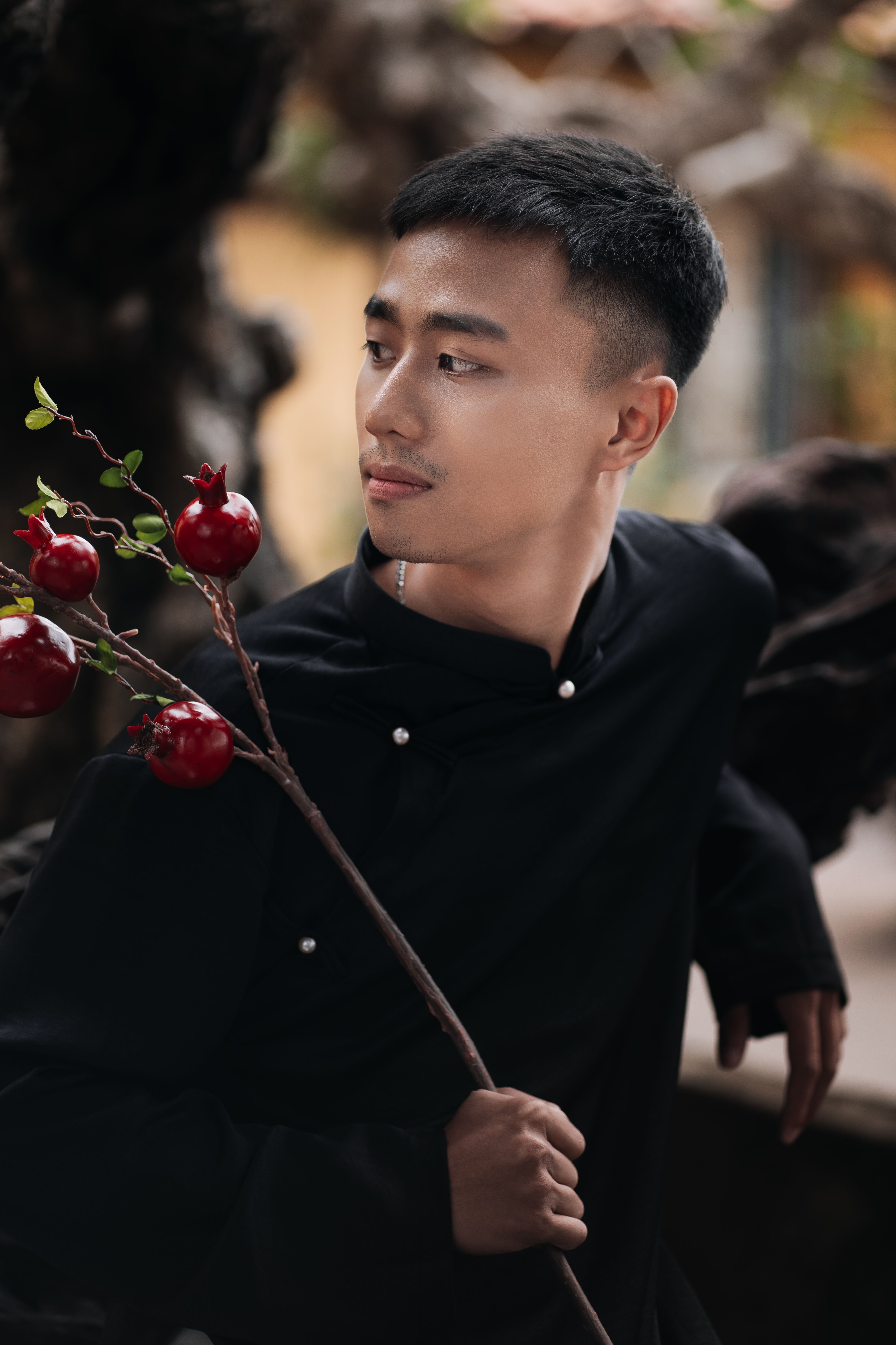 Portrait of a young man holding a pomegranate branch with an outdoor bokeh background.