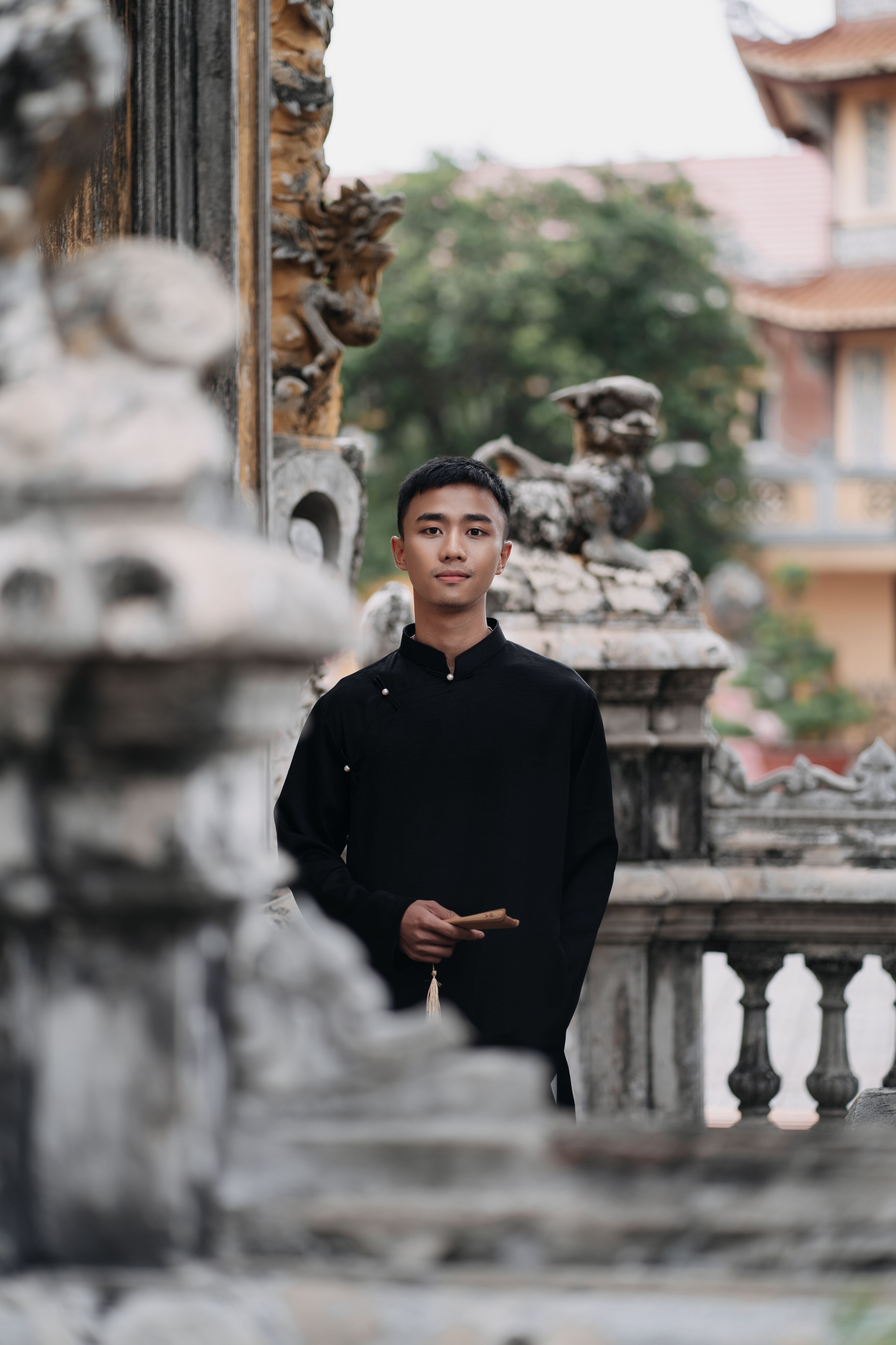 Young man in black traditional clothing standing outdoors near ancient stone architecture.
