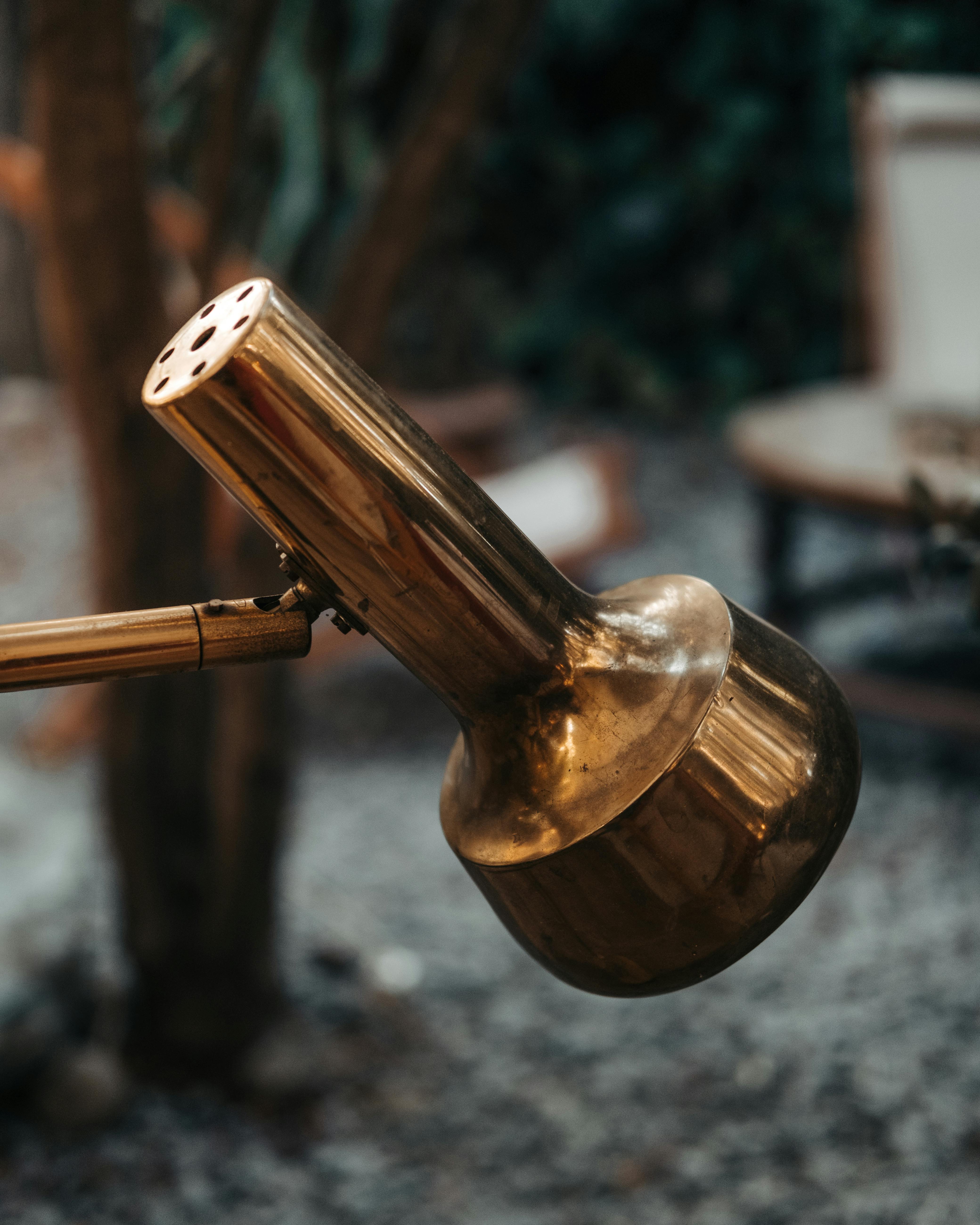 Close-up of a rustic brass watering can in an outdoor garden setting, showcasing vintage charm.