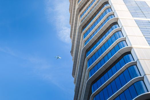 A modern skyscraper against a blue sky with an airplane flying by, showcasing urban architecture.