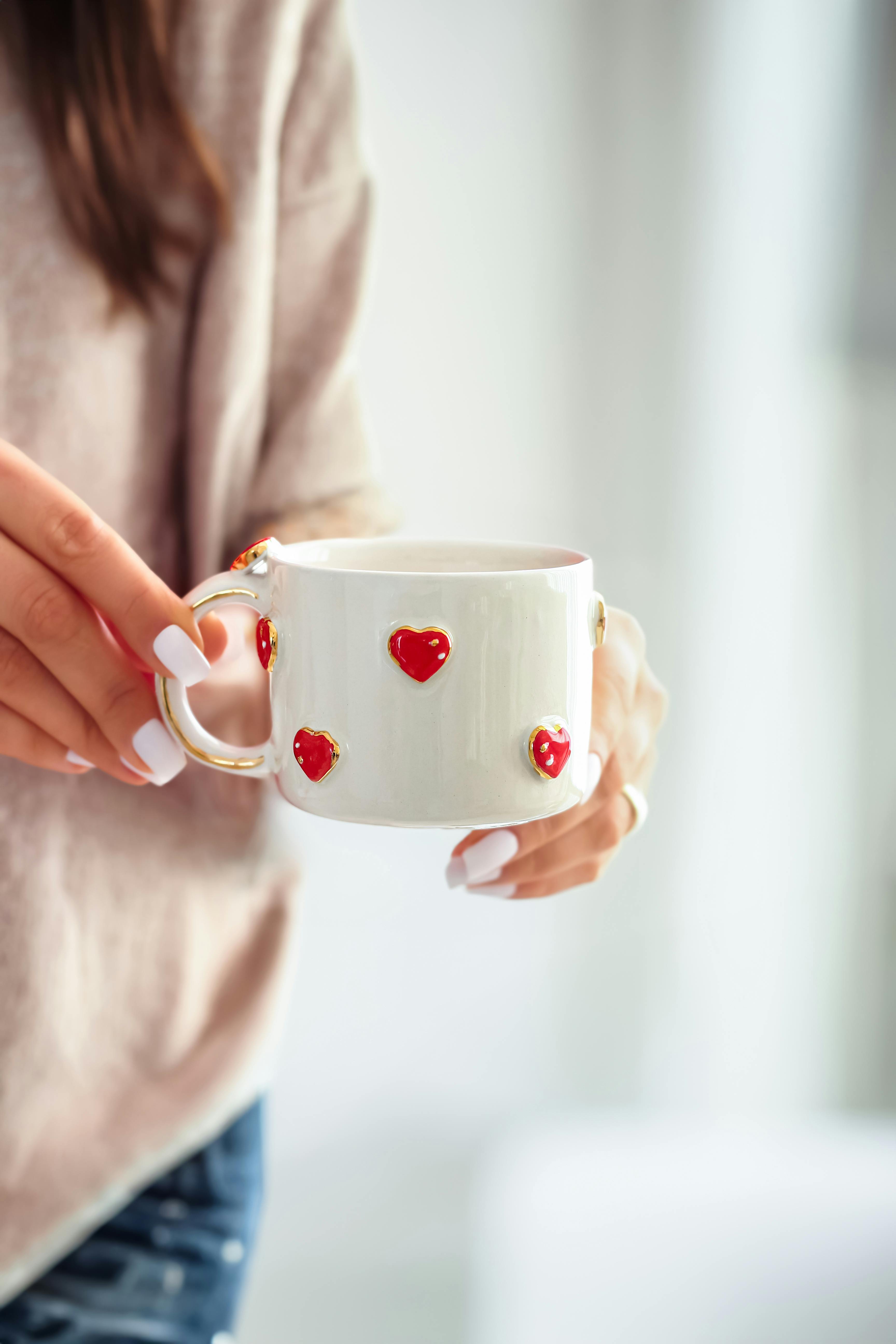 Close-up of a person holding a white mug with red hearts, evoking warmth and coziness.