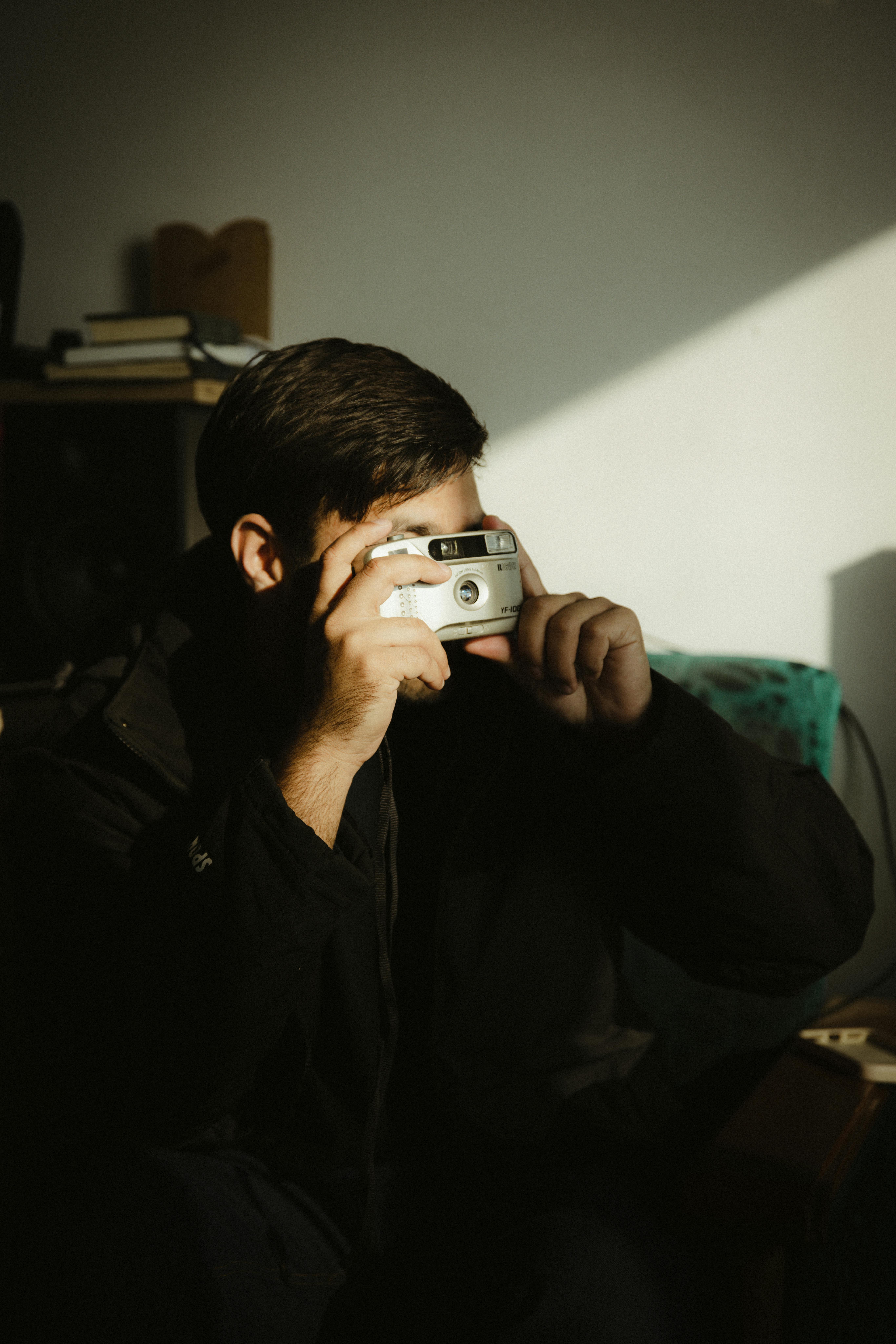 Gratis En mann som holder et filmkamera, fanget i et rom med dramatisk lys og skygger. Arkivbilde