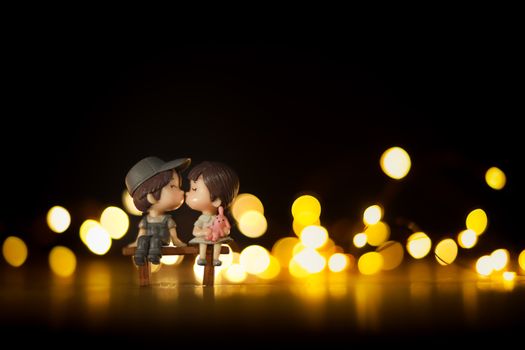 Charming miniature couple figurines on a bench with a warm bokeh light backdrop, evoking romance.
