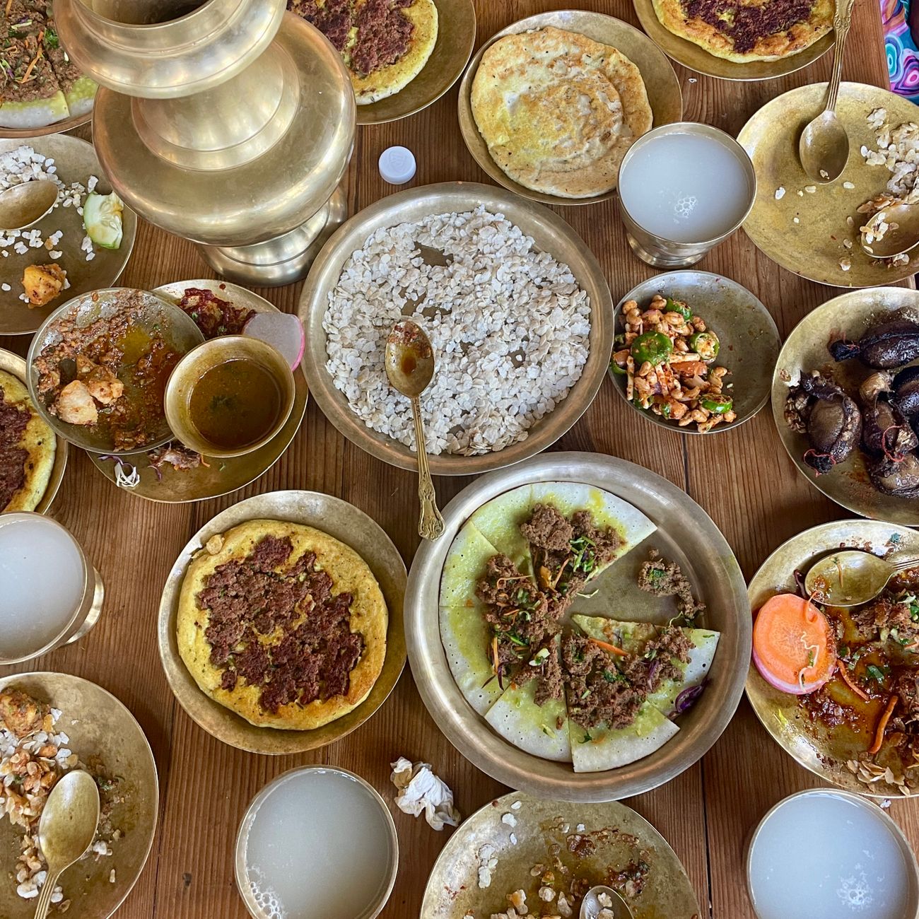 An array of Nepali dishes served in traditional brass utensils on a wooden table.