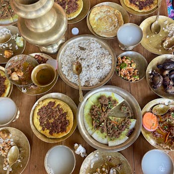 An array of Nepali dishes served in traditional brass utensils on a wooden table.