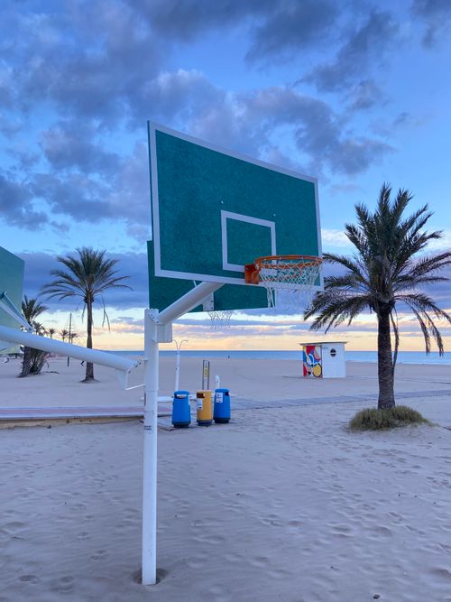 Free Outdoor basketball court at Playa de Gandía beach, Spain, with palm trees and sunset backdrop. Stock Photo