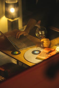 A warm, cozy workspace featuring a laptop, wine glass, and books, ideal for evening productivity.