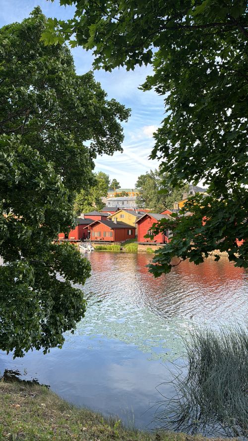 Free Scenic view of red cottages by the river in Porvoo, Finland surrounded by lush greenery. Stock Photo