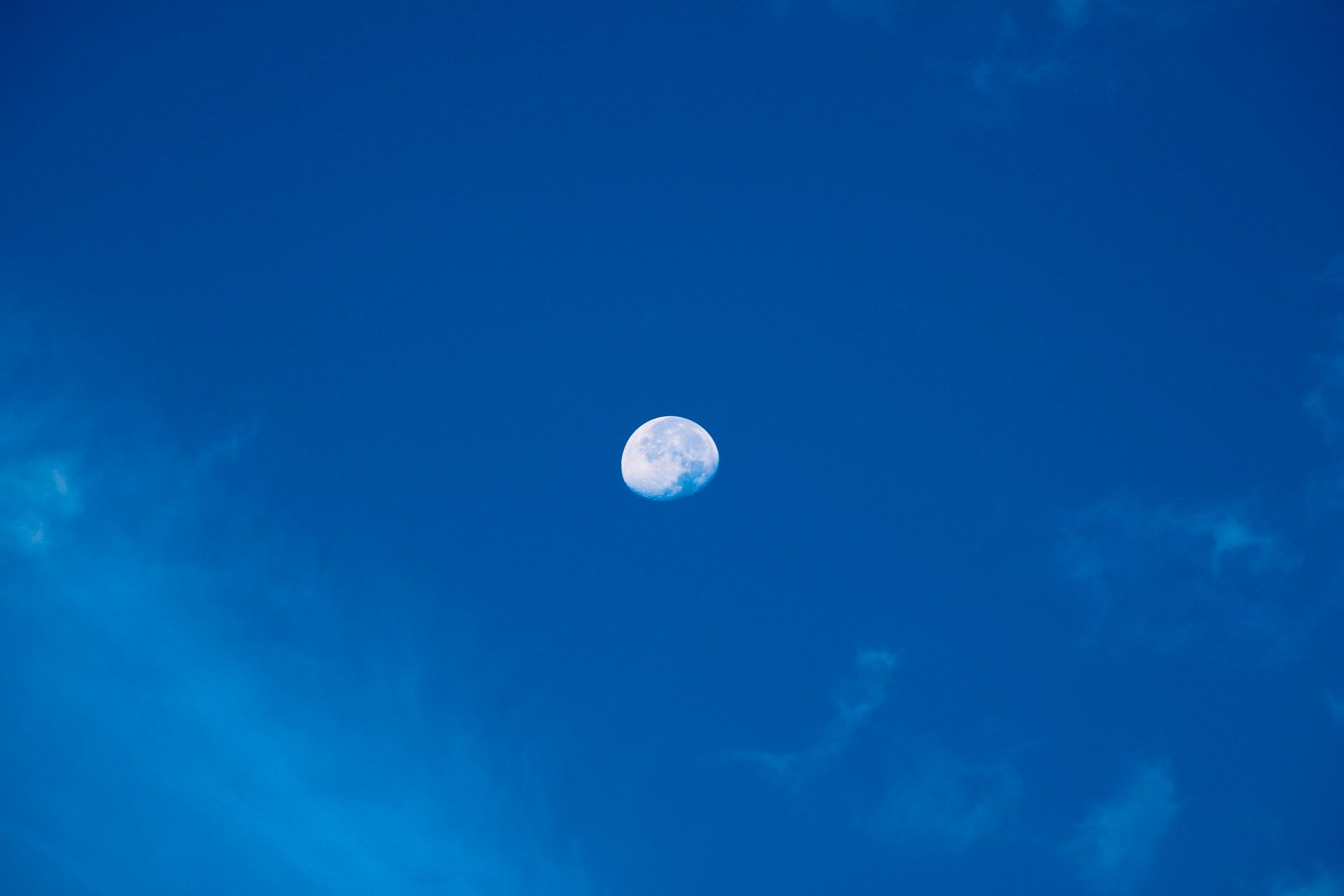 A clear view of the moon against a vivid blue sky with scattered clouds.